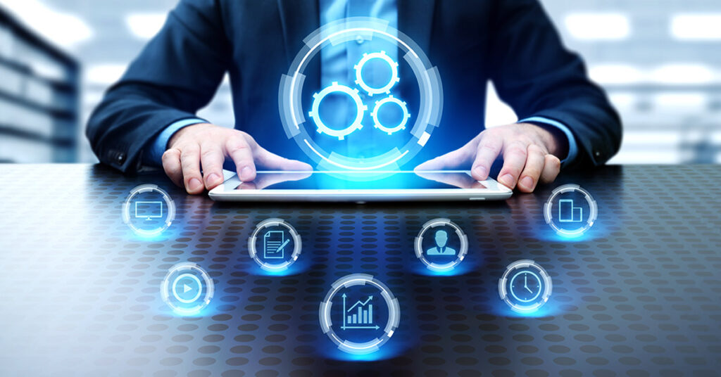 A person in a suit uses a tablet with blue, digital gears and various technology icons hovering above, symbolizing automation and digital workflow.