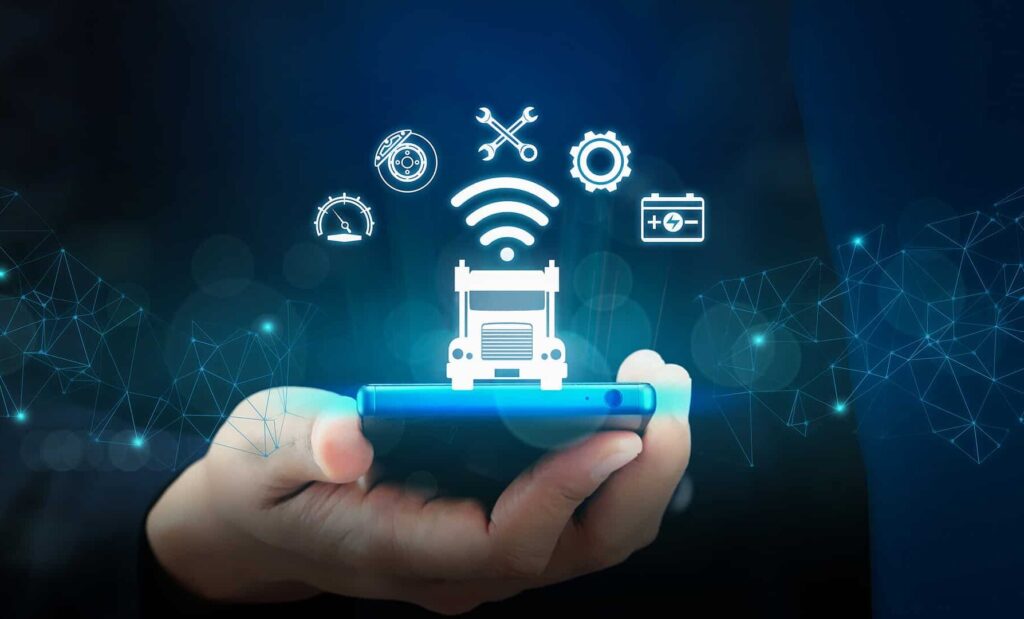 A hand holds a smartphone with glowing truck and vehicle service icons above it, representing automotive technology and digital connectivity on a dark background with abstract network graphics.