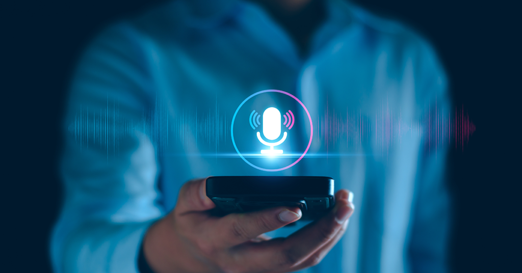 A person in a blue shirt holds a smartphone with a glowing virtual microphone icon and sound wave graphics, representing voice assistant technology.
